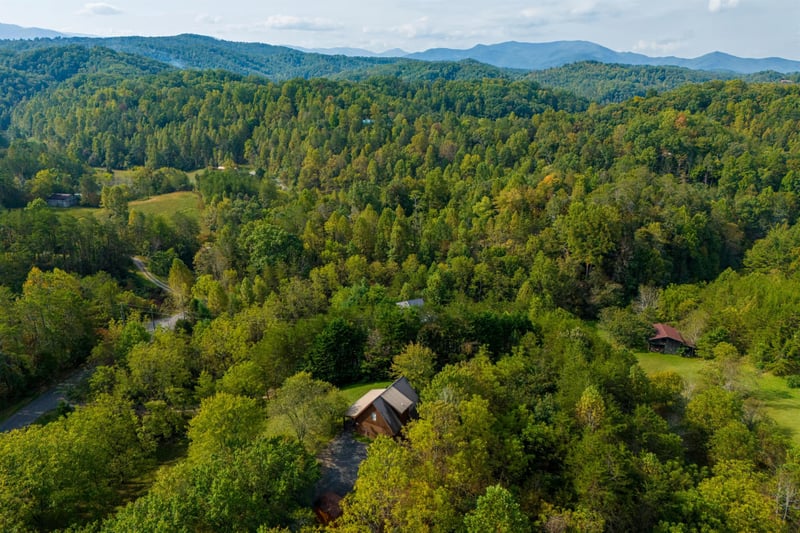 Spectacular aerial view showcases the property nestled among rolling mountain ridges and dense forest canopy in this pristine natural setting.