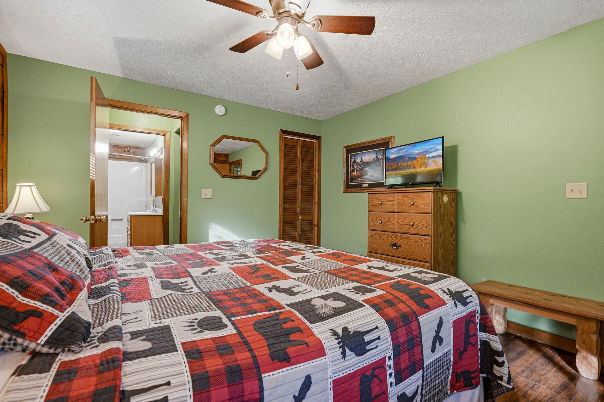 Unwind in your cozy bedroom with rustic charm, featuring warm green walls, wooden furnishings, and a ceiling fan for your comfort.