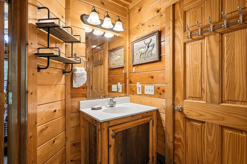 Rustic charm meets functionality in this cozy cabin bathroom, featuring warm wood paneling, convenient storage shelves, and wildlife artwork to enhance your mountain retreat experience.