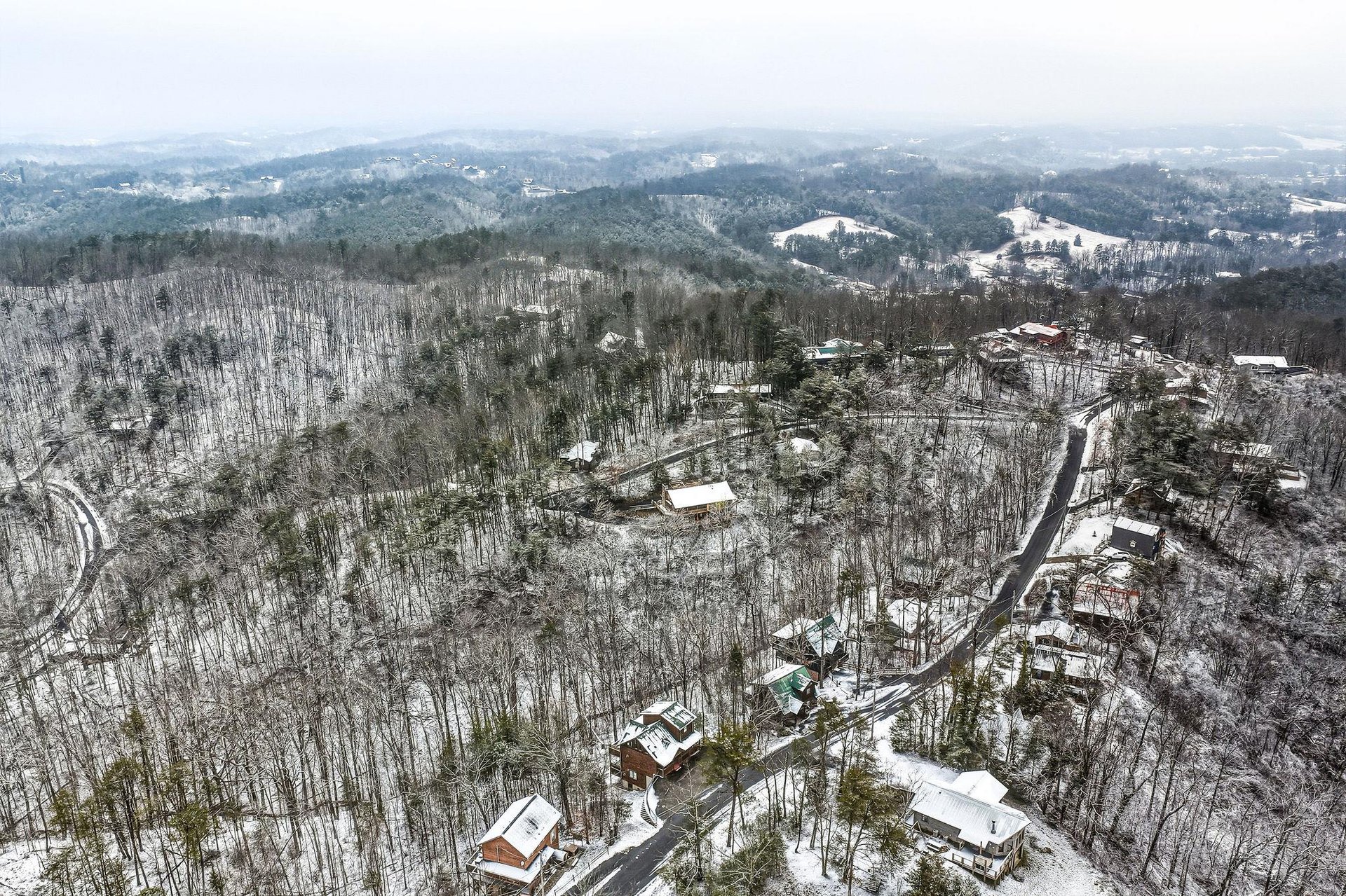 Aerial winter view showcasing the peaceful neighborhood nestled among snowcovered hills and bare trees.