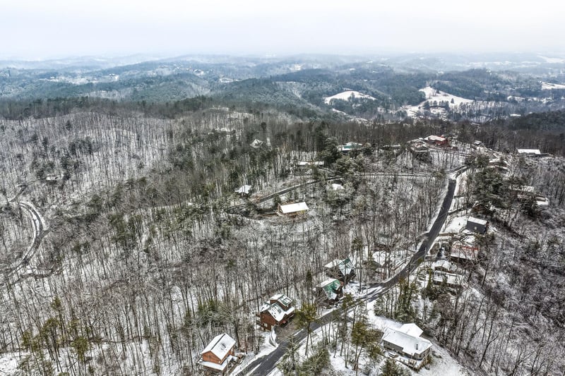 Aerial winter view showcasing the peaceful neighborhood nestled among snowcovered hills and bare trees.