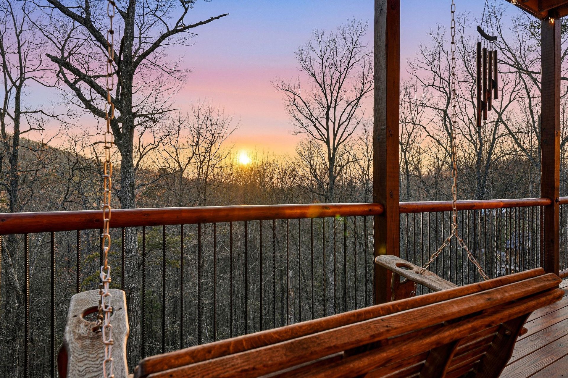 Stunning sunset paints the sky in soft pastels beyond this elevated deck, creating a perfect backdrop for the peaceful wooded setting.