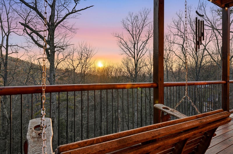 Stunning sunset paints the sky in soft pastels beyond this elevated deck, creating a perfect backdrop for the peaceful wooded setting.