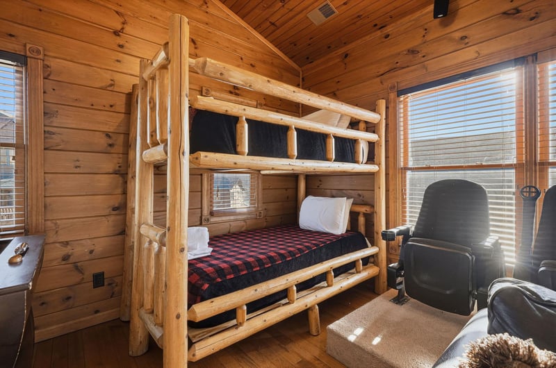 Rustic log bunk beds with plaid bedding create a cozy mountain retreat vibe. Large windows flood your space with natural light, while leather seating invites relaxation after adventurefilled days.