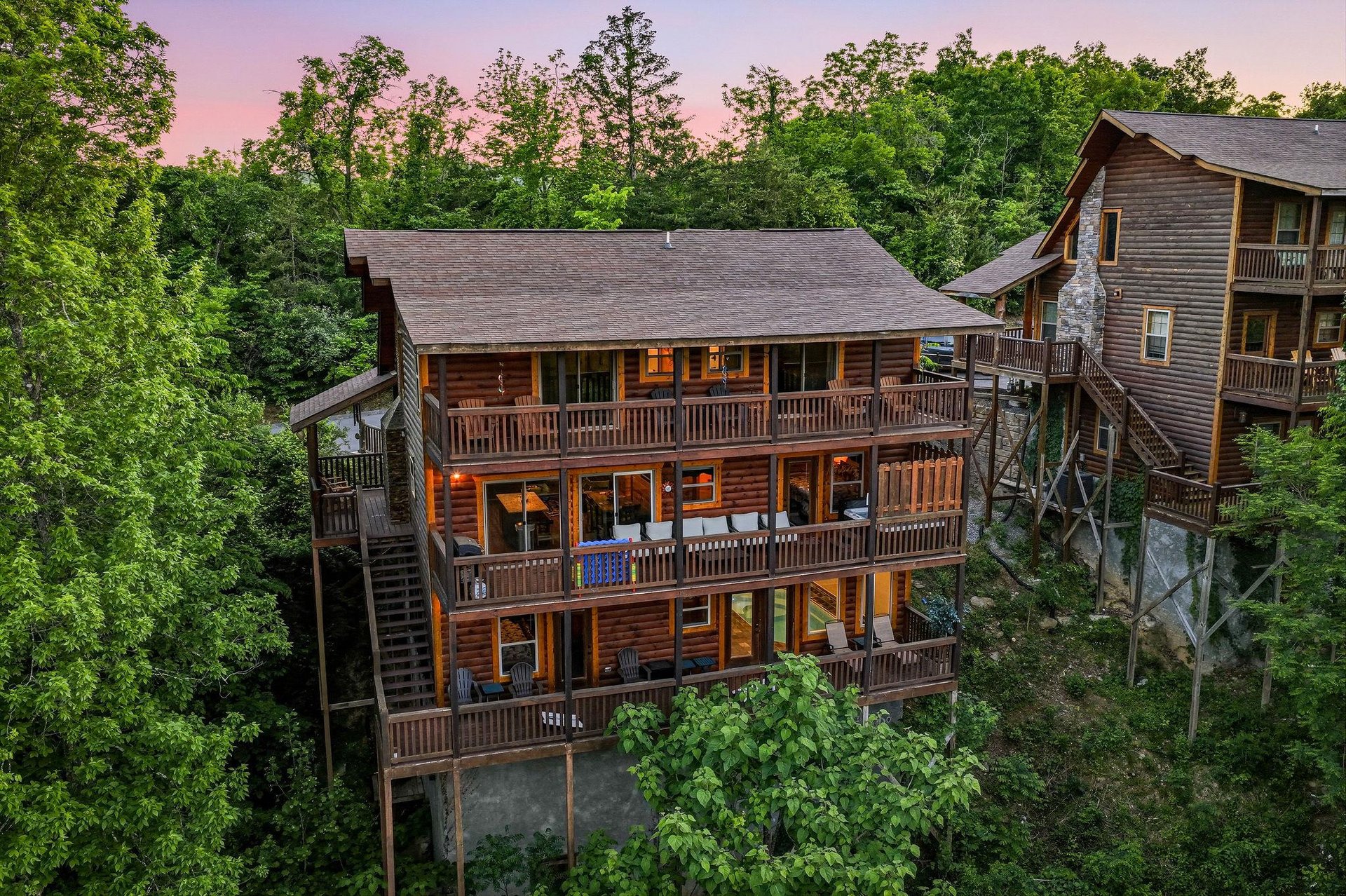 Multilevel cabin nestled among lush forest trees with pink sunset sky painting the evening horizon beautifully.