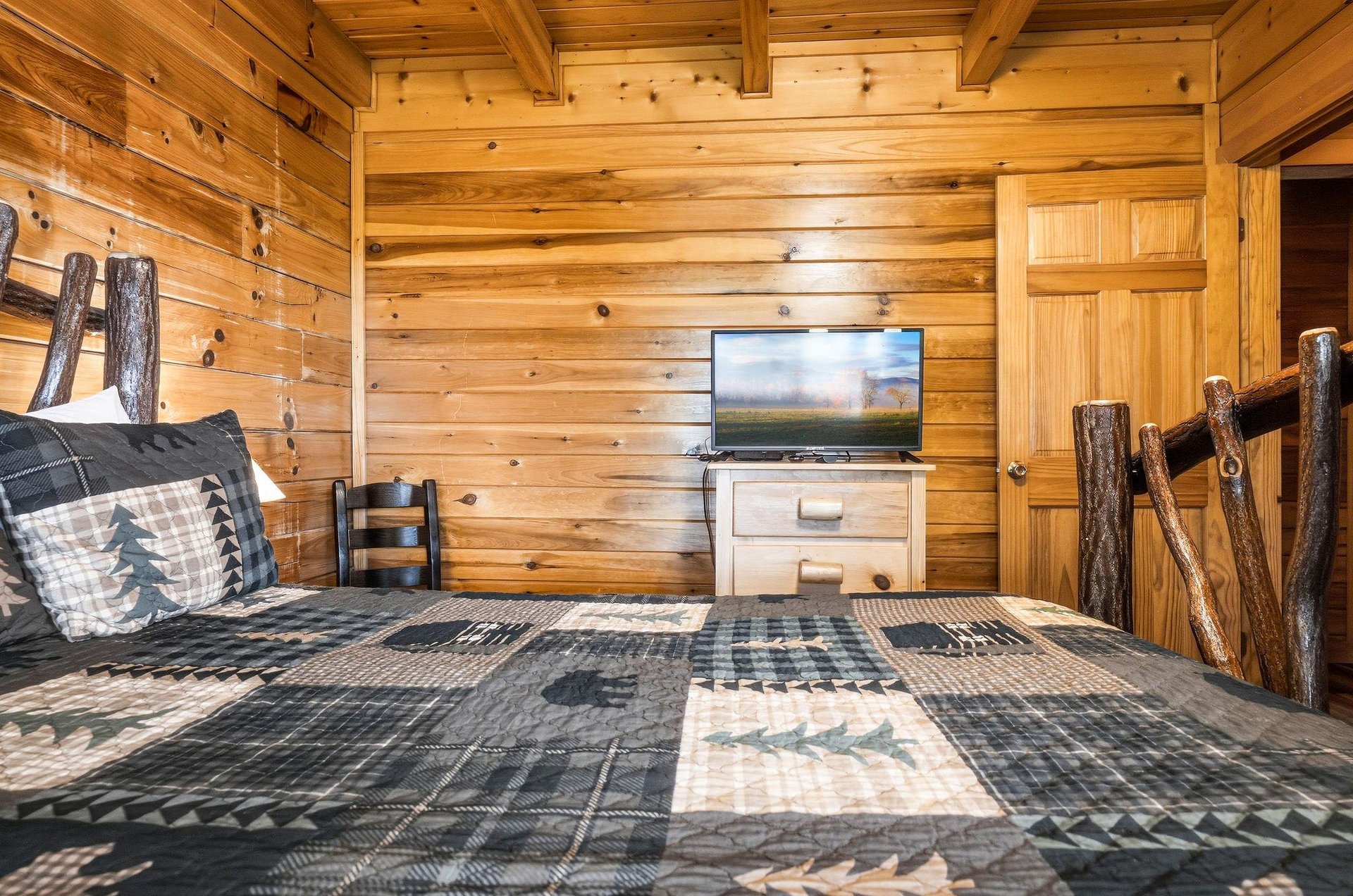 Cozy rustic bedroom with warm pine walls, handcrafted log bed frame, and modern TV for your entertainment. Relax in this charming cabinstyle retreat with natureinspired décor.