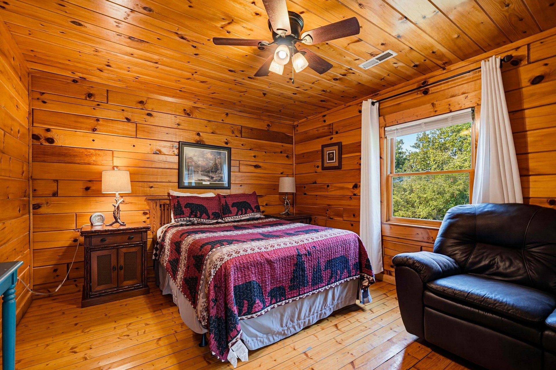 Wake up in this warm, rustic bedroom where knotty pine walls and a soft quilted bed create your cozy cabin retreat. Natural light streams through the window, inviting you to start your day refreshed.