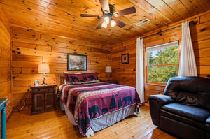 Wake up in this warm, rustic bedroom where knotty pine walls and a soft quilted bed create your cozy cabin retreat. Natural light streams through the window, inviting you to start your day refreshed.