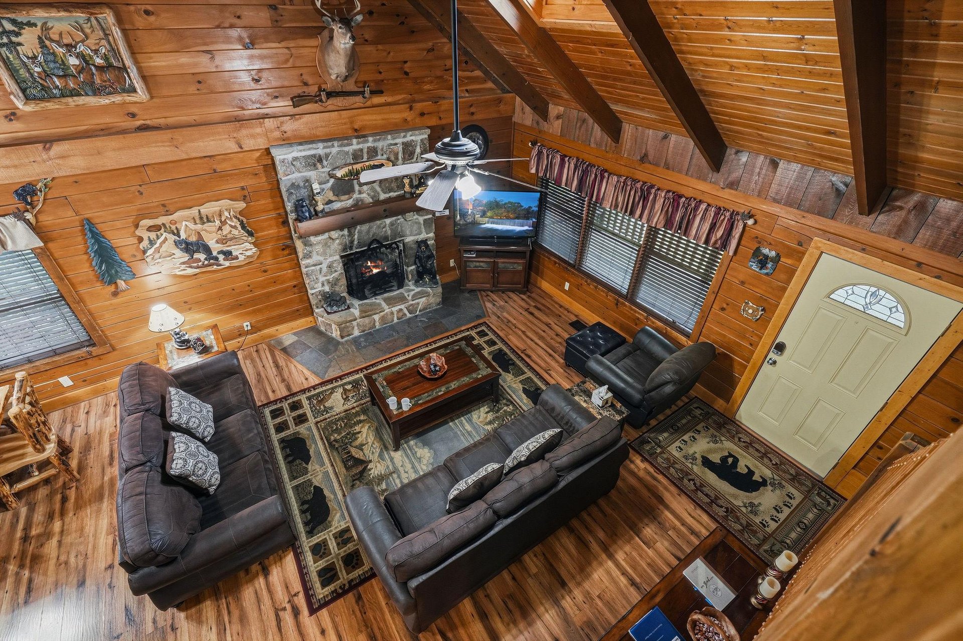 Your spacious cabin living room invites you to relax by the stone fireplace beneath soaring woodbeamed ceilings. Plush leather sofas and rustic décor create the perfect cozy retreat after a day outdo