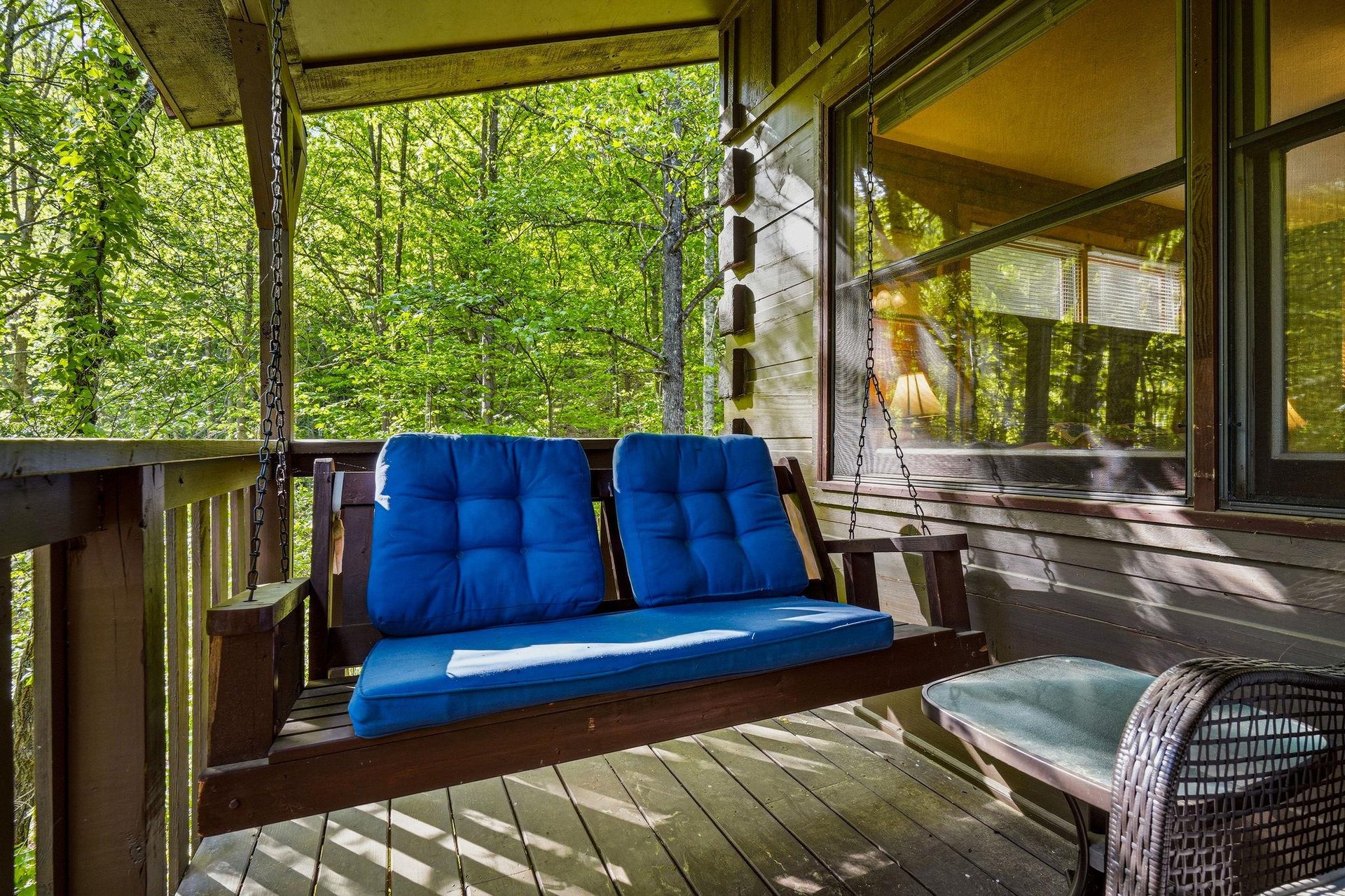 Unwind on your private porch swing with plush blue cushions, surrounded by peaceful forest views through towering trees.