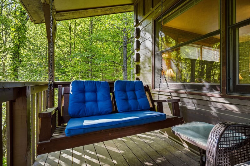 Unwind on your private porch swing with plush blue cushions, surrounded by peaceful forest views through towering trees.