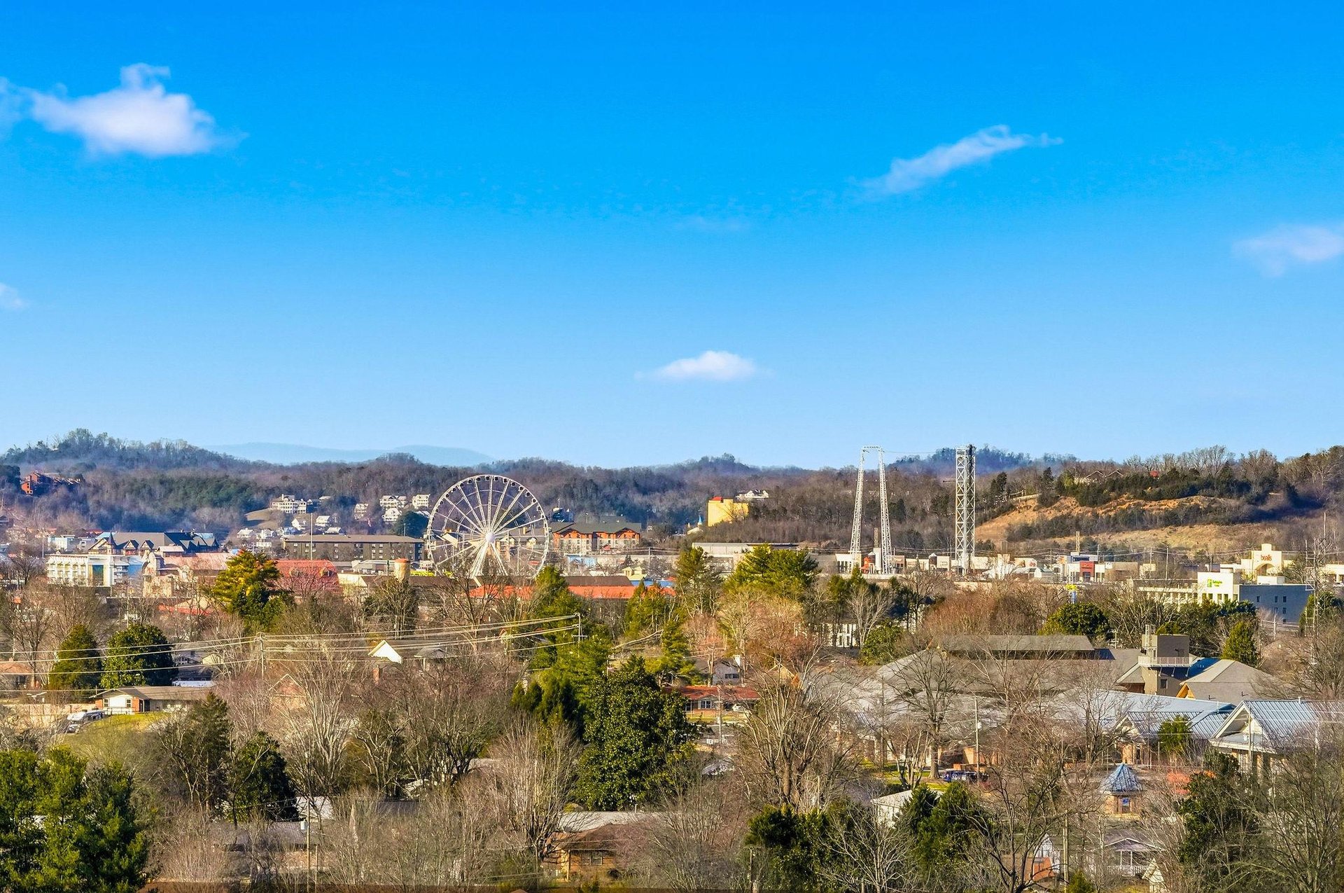 Scenic city view featuring a prominent Ferris wheel and rolling hills under bright blue skies.