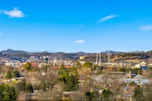 Scenic city view featuring a prominent Ferris wheel and rolling hills under bright blue skies.