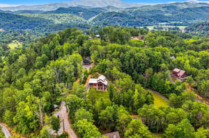 Aerial view showcasing the property nestled among lush forest and rolling hills, with sweeping mountain vistas extending across the horizon in the surrounding area.