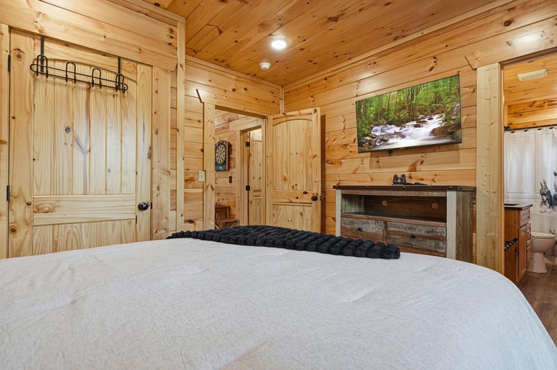 Retreat to your cozy bedroom with rustic pine walls, a plush bed, and a peaceful nature scene on the TV to help you unwind after a day of adventure.