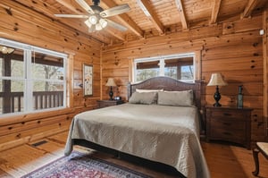 Drift off in your cozy log cabin bedroom with rustic charm and peaceful forest views through large windows.