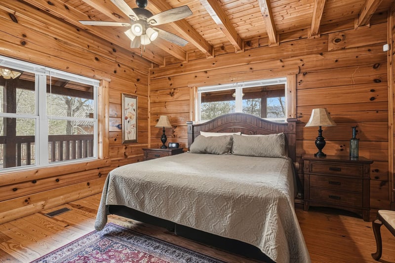 Drift off in your cozy log cabin bedroom with rustic charm and peaceful forest views through large windows.