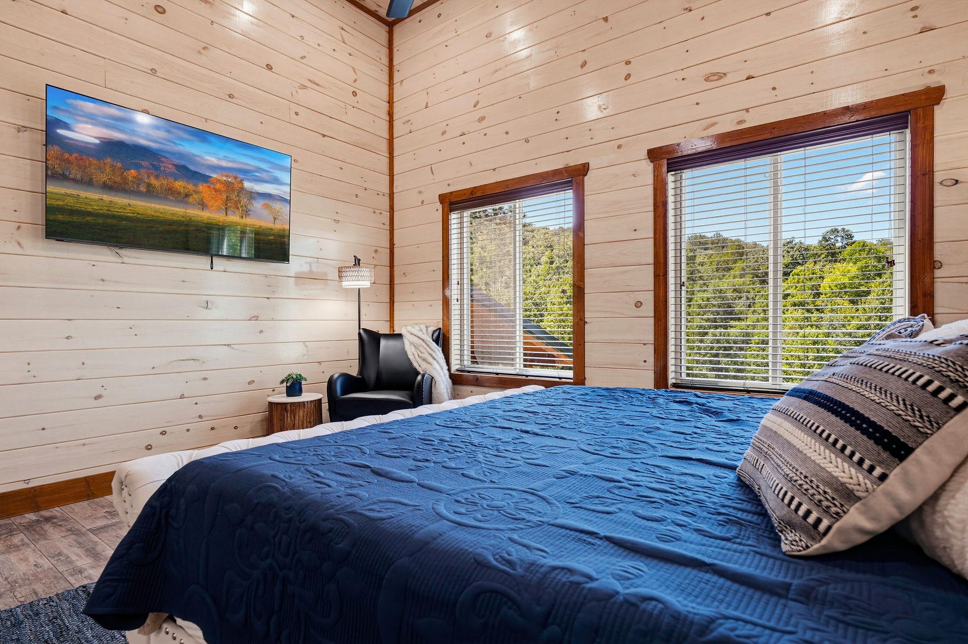 Wake up to bright natural light streaming through large windows, showcasing lush greenery beyond. The warm pine walls and plush bedding create a cozy retreat where you can truly unwind.