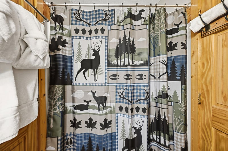 Step into a cozy retreat where rustic pine walls frame your inviting bed and towelready hooks, while a naturethemed shower curtain adds woodland charm to your private bathroom.