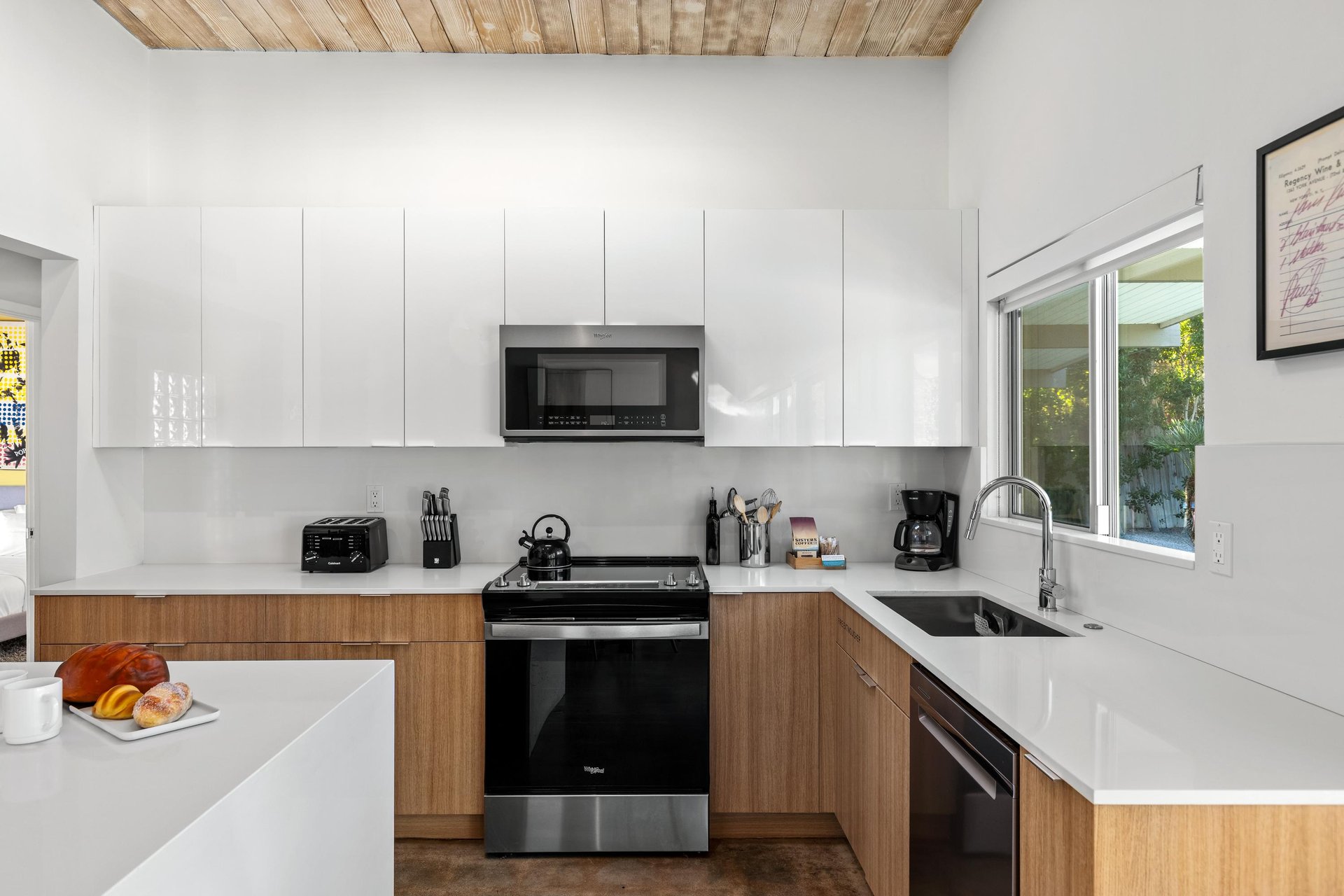 Your sleek modern kitchen features white quartz counters, full appliances, and warm wood accents under gorgeous exposed beam ceilings.