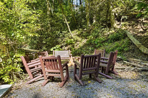 Gather around the rustic wooden fire pit circle, nestled against the tranquil backdrop of towering trees and natural woodlands. Perfect for evening storytelling or morning coffee.