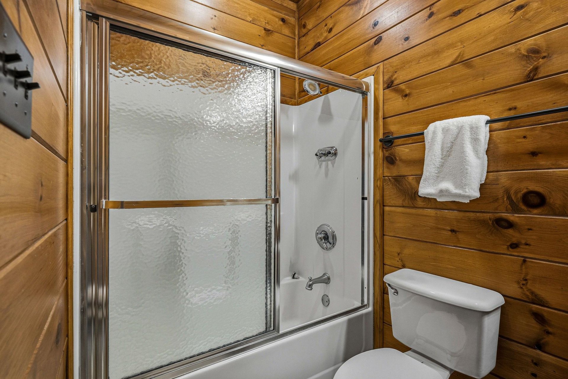 Freshen up in your cozy cabin bathroom featuring a tubshower combo with warm wood plank walls and plush towels waiting for you.