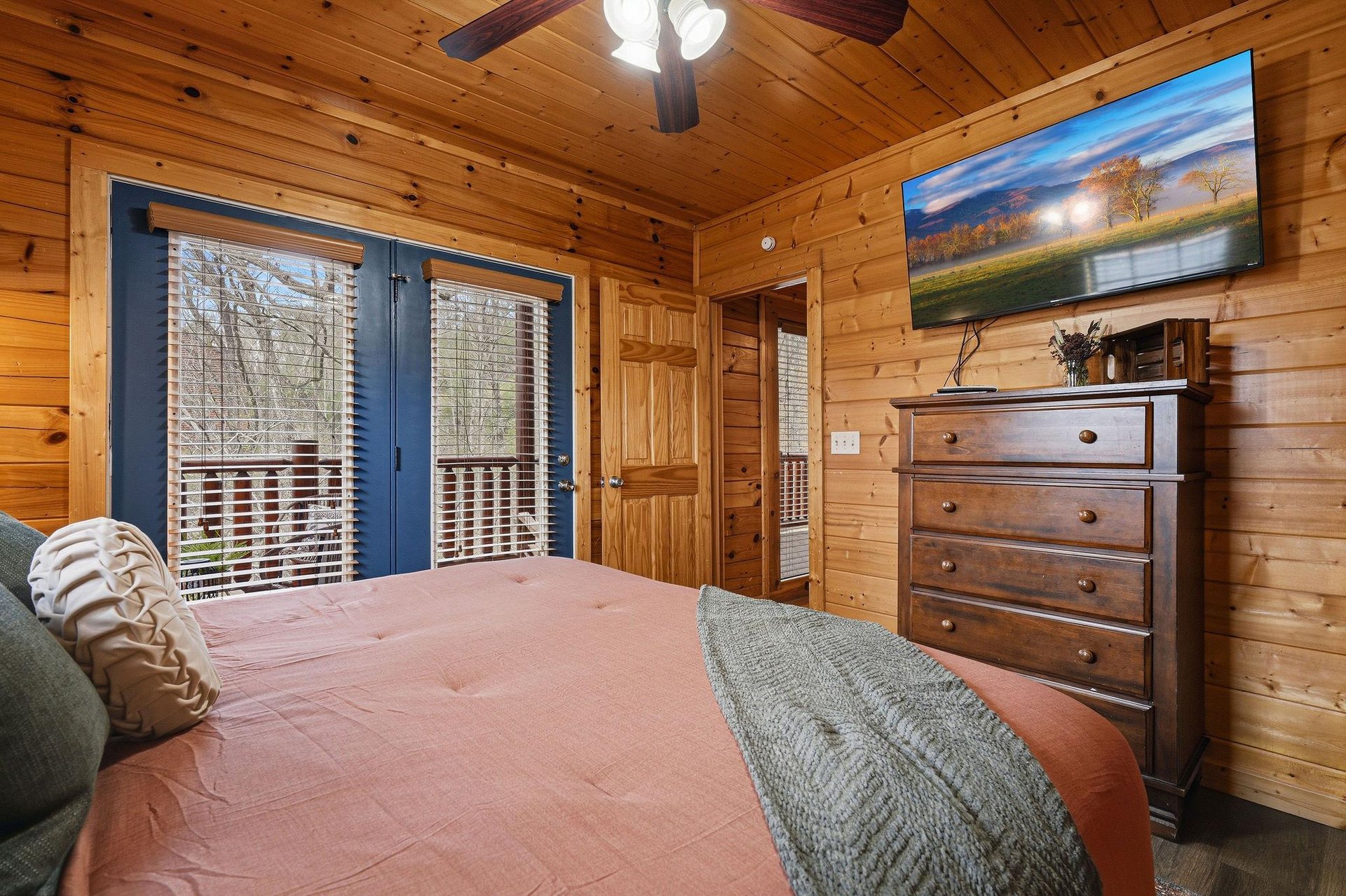 Cozy cabin bedroom with rustic wood walls, comfortable bedding, and private balcony access for your peaceful mountain retreat.