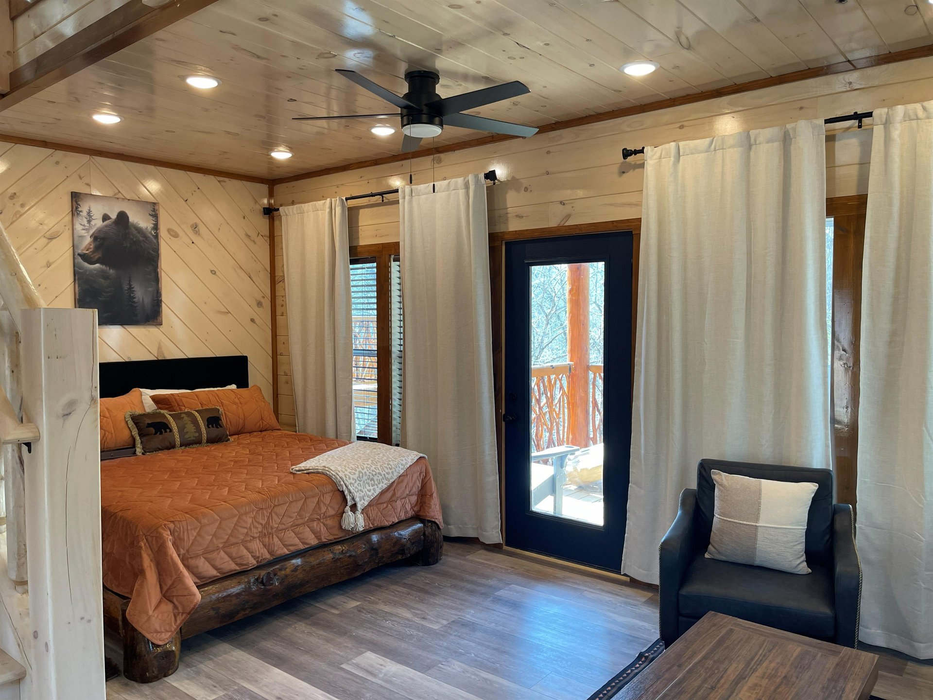 Unwind in your cozy rustic bedroom with warm wood accents, comfortable seating, and private balcony access for peaceful moments.