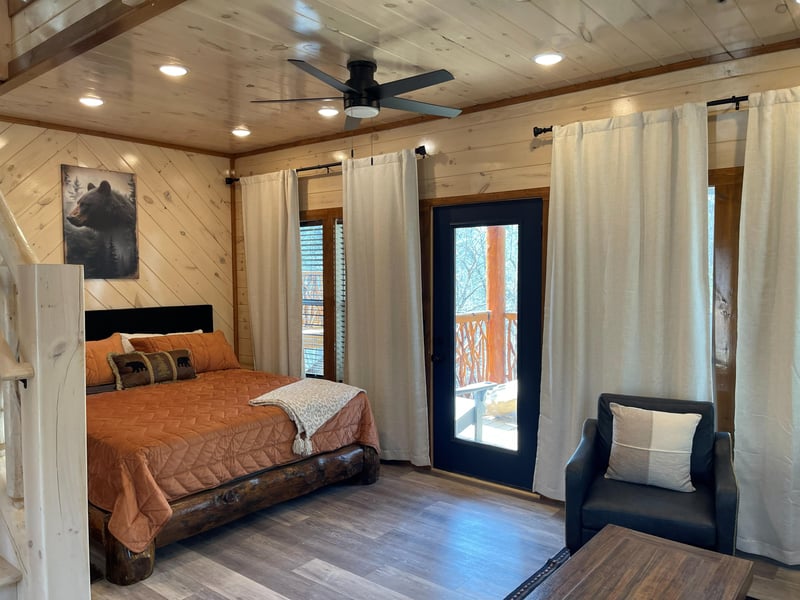 Unwind in your cozy rustic bedroom with warm wood accents, comfortable seating, and private balcony access for peaceful moments.