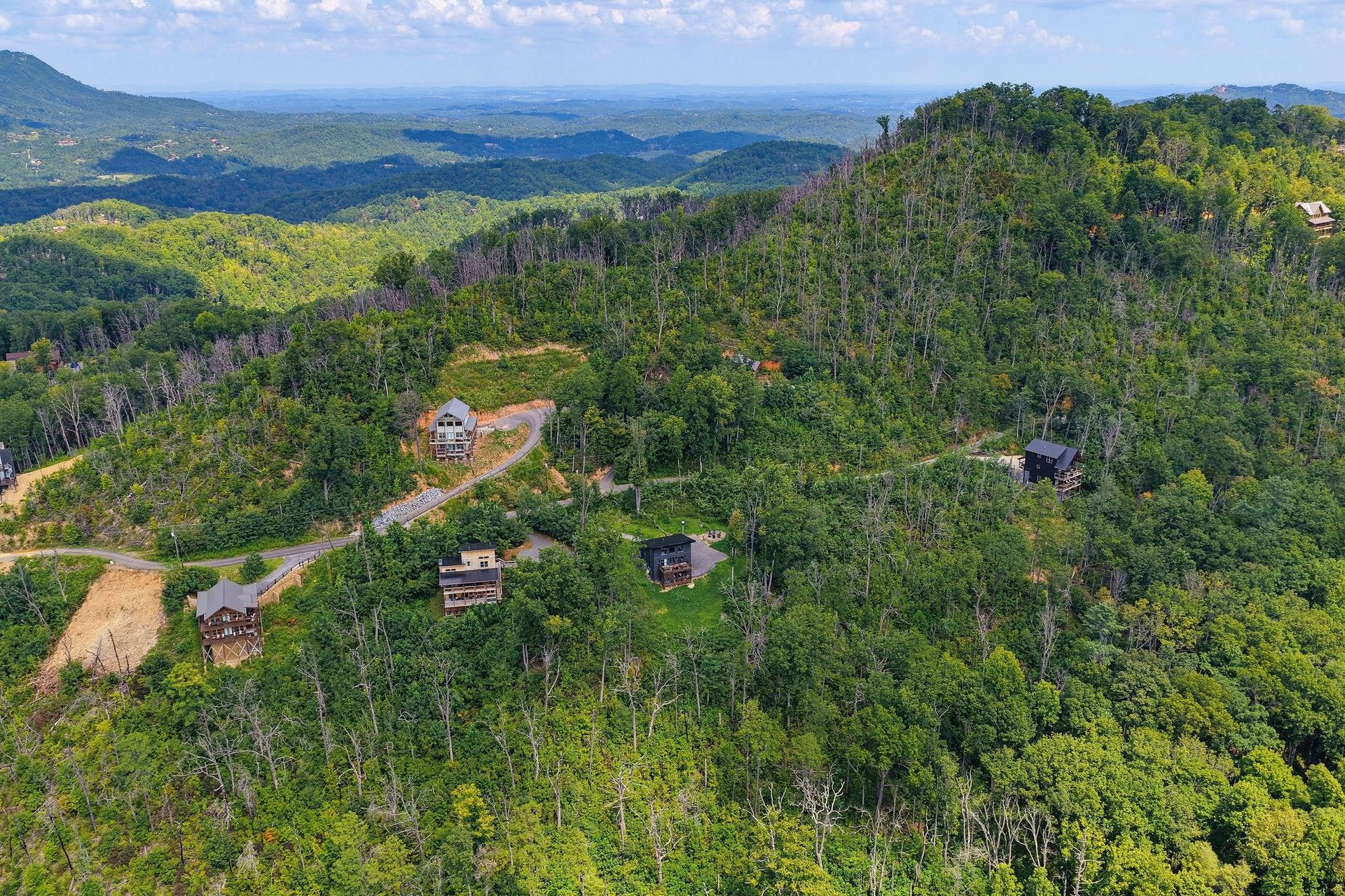 Aerial view shows the rental property nestled in a lush forested mountainside with sweeping natural landscapes stretching to the horizon.