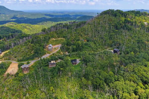Aerial view shows the rental property nestled in a lush forested mountainside with sweeping natural landscapes stretching to the horizon.