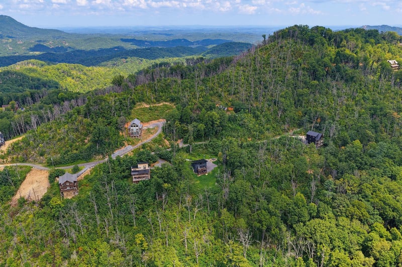 Aerial view shows the rental property nestled in a lush forested mountainside with sweeping natural landscapes stretching to the horizon.
