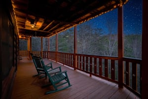Your private deck invites peaceful stargazing moments in comfortable rocking chairs, where twinkling lights frame stunning forest views beneath the night sky.