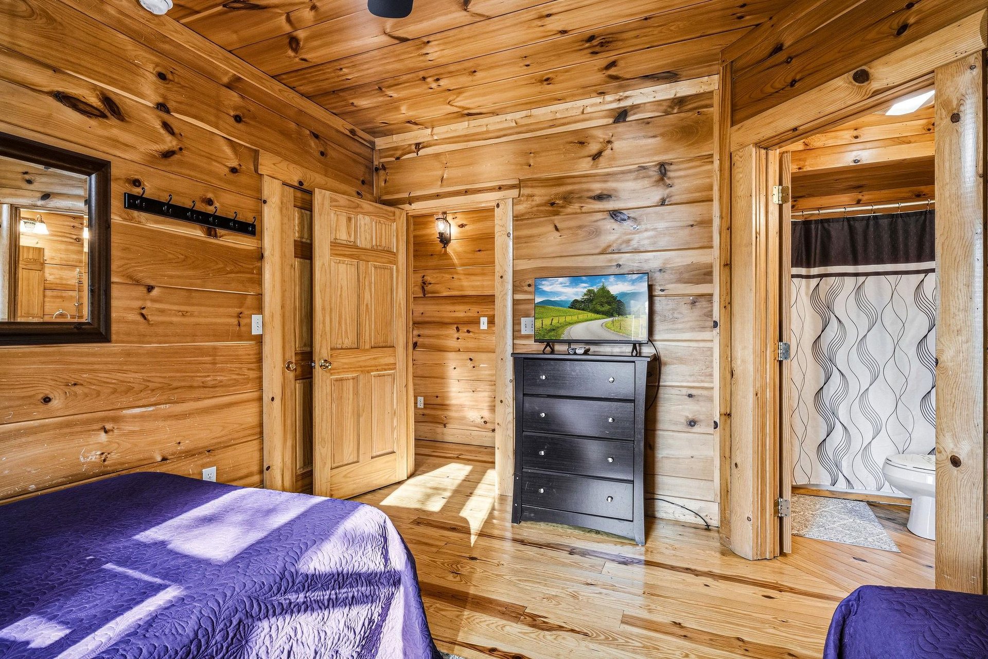 Embrace rustic charm in your woodpaneled bedroom with TV entertainment, private bathroom access, and natural light filtering through windows.