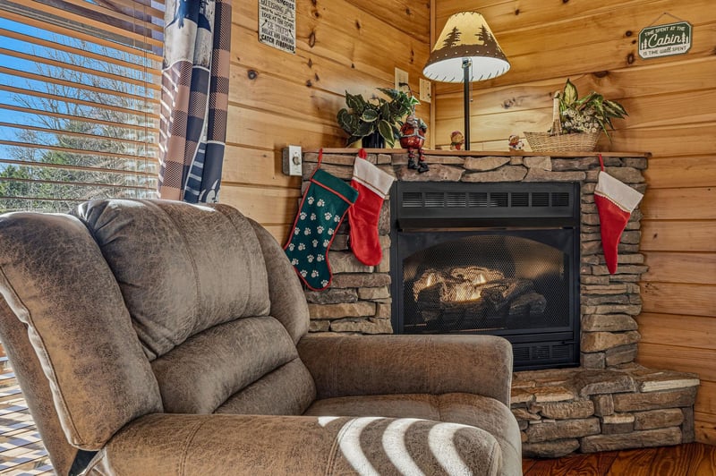 Cozy up in your plush recliner beside the crackling stone fireplace, where stockings hang and warm cabin vibes embrace you.