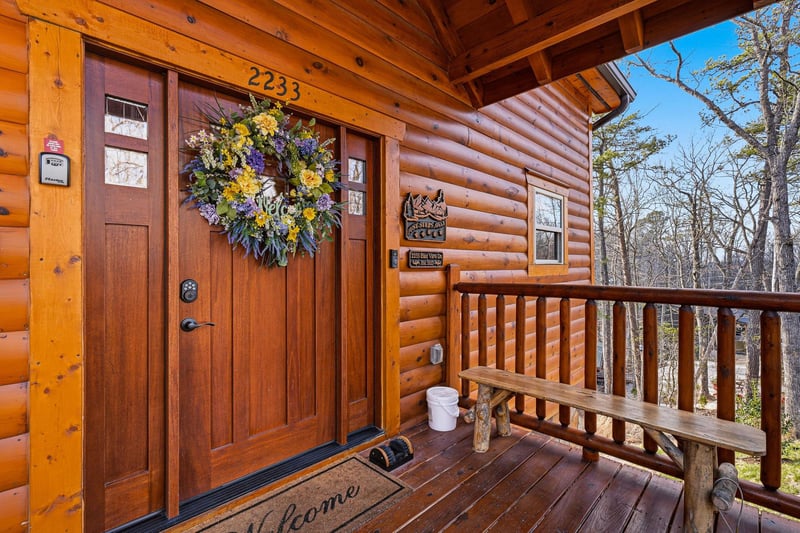 Charming log cabin entrance welcomes you with rustic warmth and mountain views from your private covered porch.