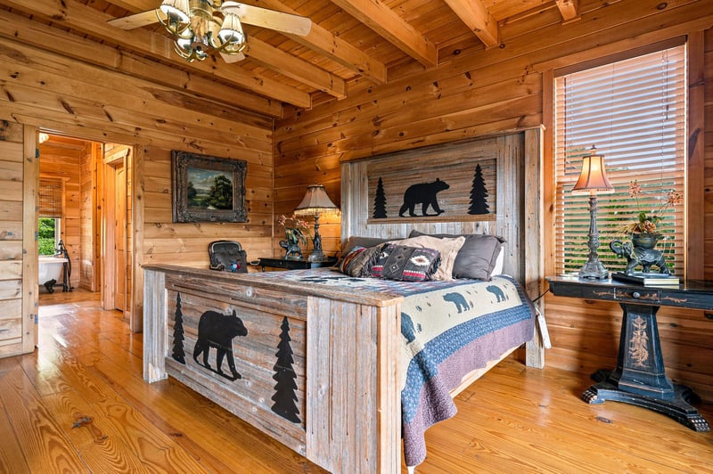 Unwind in your cozy, cabinstyle bedroom with warm wood beams, rustic bearthemed décor, and peaceful views through the window.