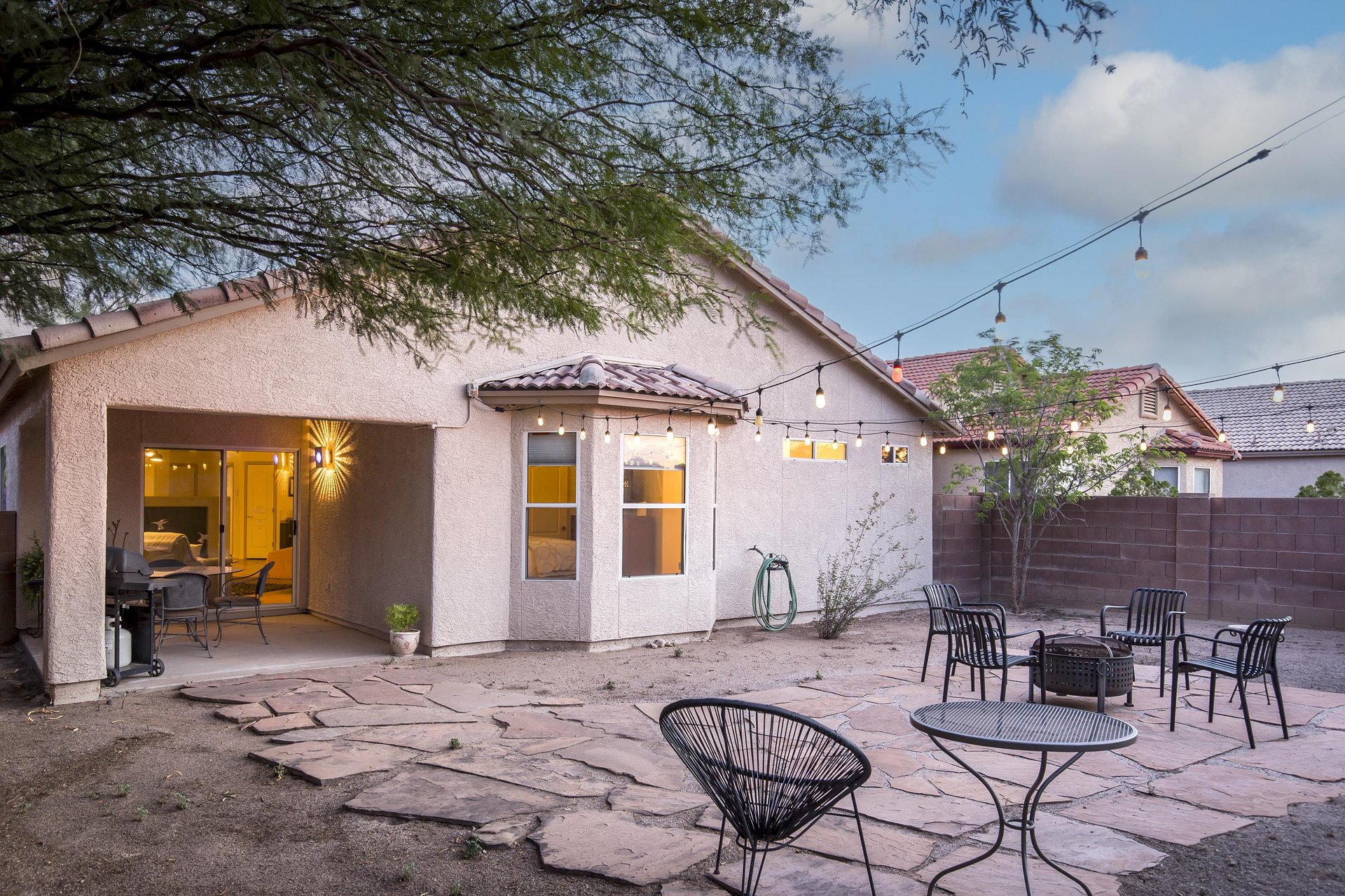 Just off the back patio is the fully enclosed outdoor space with string lights, a fire pit, and additional outdoor seating.