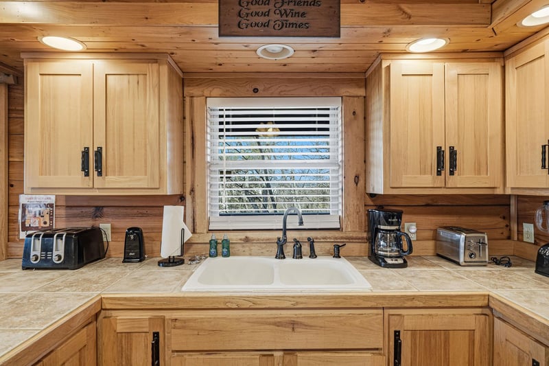 Your rustic kitchen features warm wood cabinets and modern appliances, perfect for preparing meals while enjoying natural light streaming through the window.