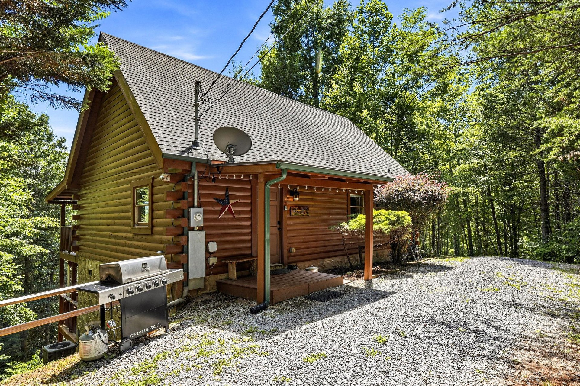 Charming log cabin nestled in wooded surroundings with gravel parking and outdoor grill for your mountain getaway.