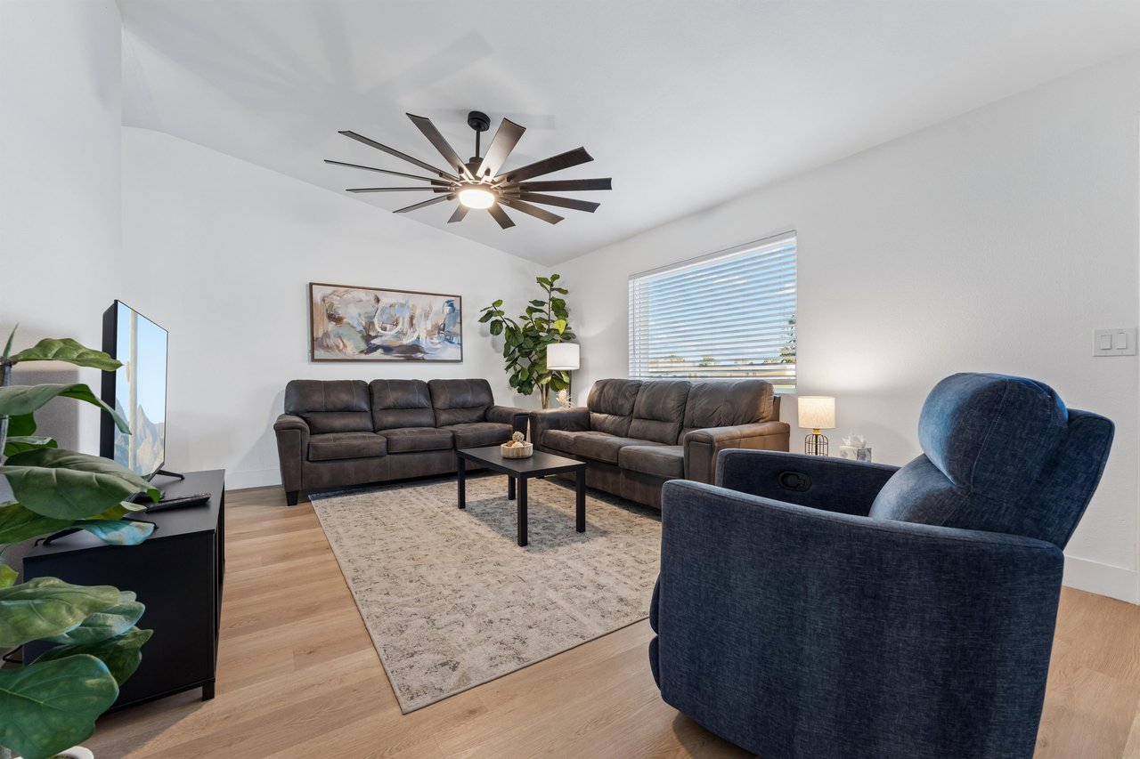 Spacious living room with a flatscreen TV, ample seating, and a large ceiling fan.