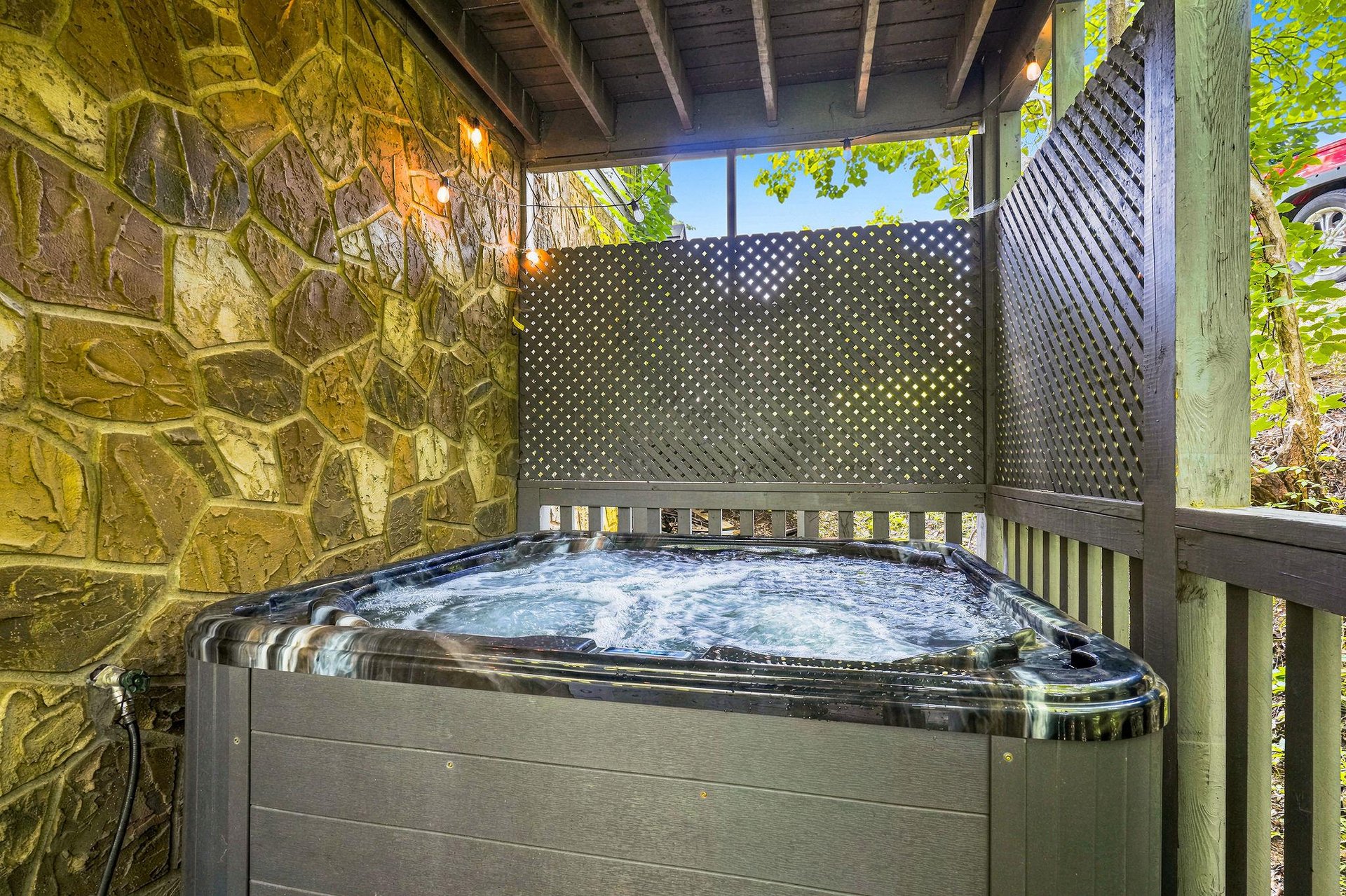 Slip into the bubbling hot tub on your private covered terrace, where warm string lights and stone accent walls create a cozy retreat after a day of exploring.
