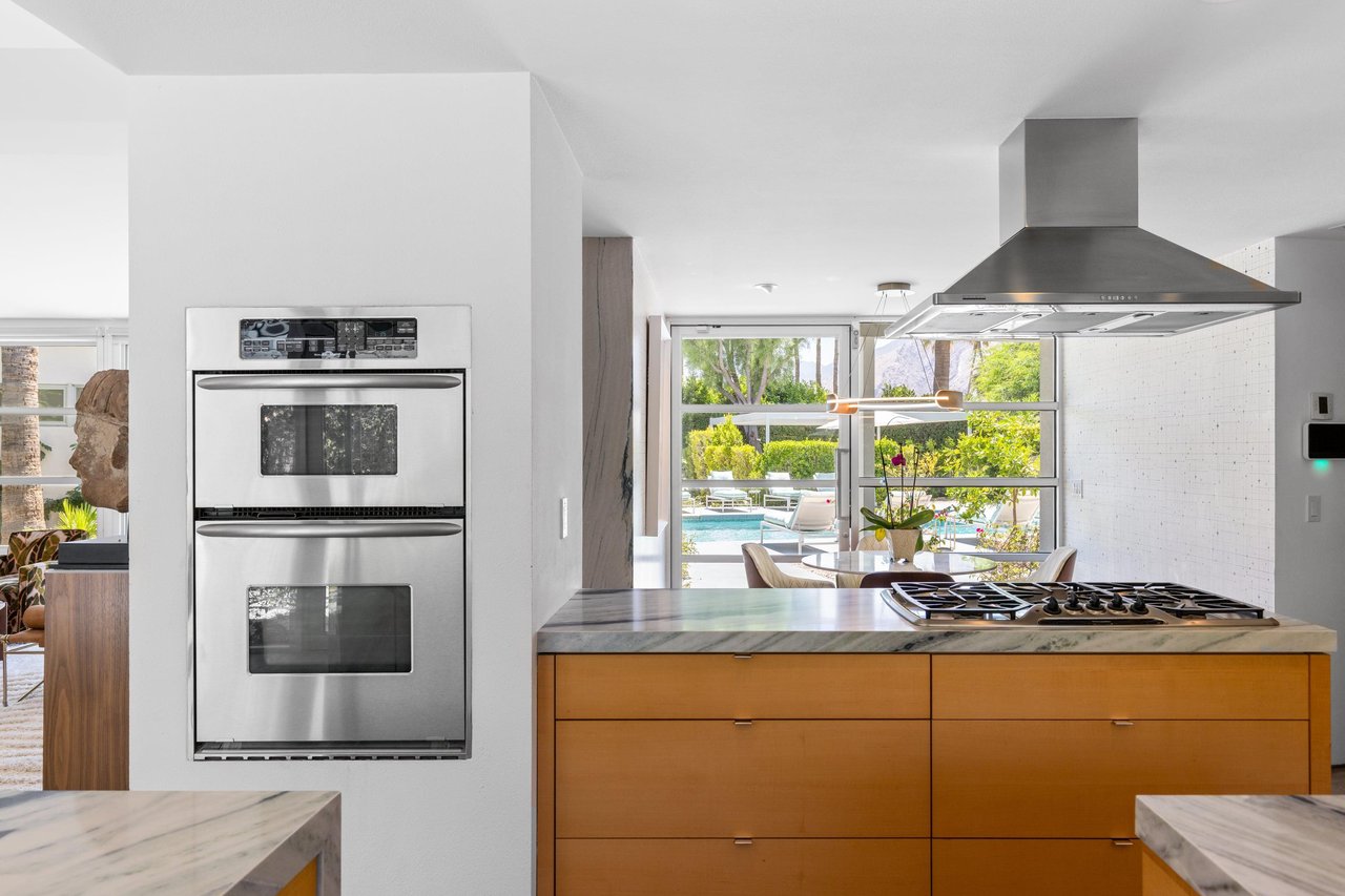Modern chefs kitchen with a waterfall marble counter, kitchen island, stainlesssteel appliances, wine fridge, wet bar, and kitchen essentials. On the other side of the stove is where the breakfast nook can be found.
