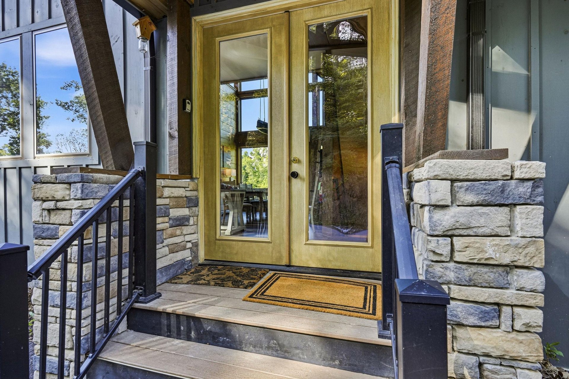 The welcoming entrance greets you with sturdy stonework and glass doors that reveal glimpses of the bright interior and surrounding natural beauty beyond.
