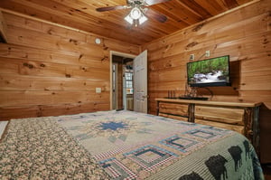 Unwind in your cozy cabin bedroom featuring warm pine walls, rustic log furnishings, and a ceiling fan for comfort. Enjoy your favorite shows on the flatscreen TV after exploring the outdoors.