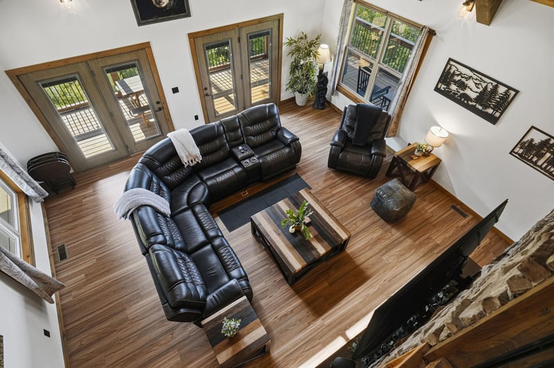 Spacious sunfilled living room with soaring ceilings, plush leather seating, and rustic wood floors. French doors open to a private deck, while a stone fireplace creates the perfect retreat.