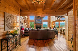 Warm wooden beams and a stone fireplace create a cozy retreat where you can relax on plush sofas and gaze out at stunning mountain views framing the horizon.