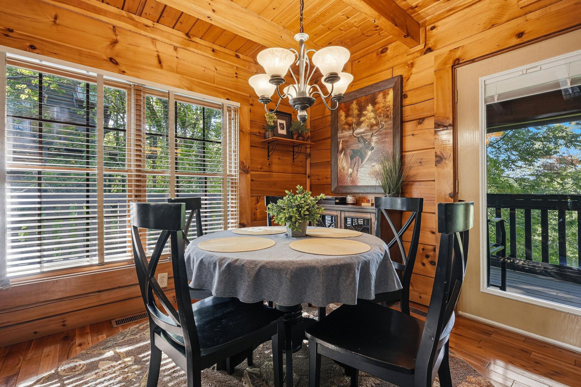 Your rustic dining nook features warm wood beams, elegant chandelier lighting, and peaceful forest views through large windows.