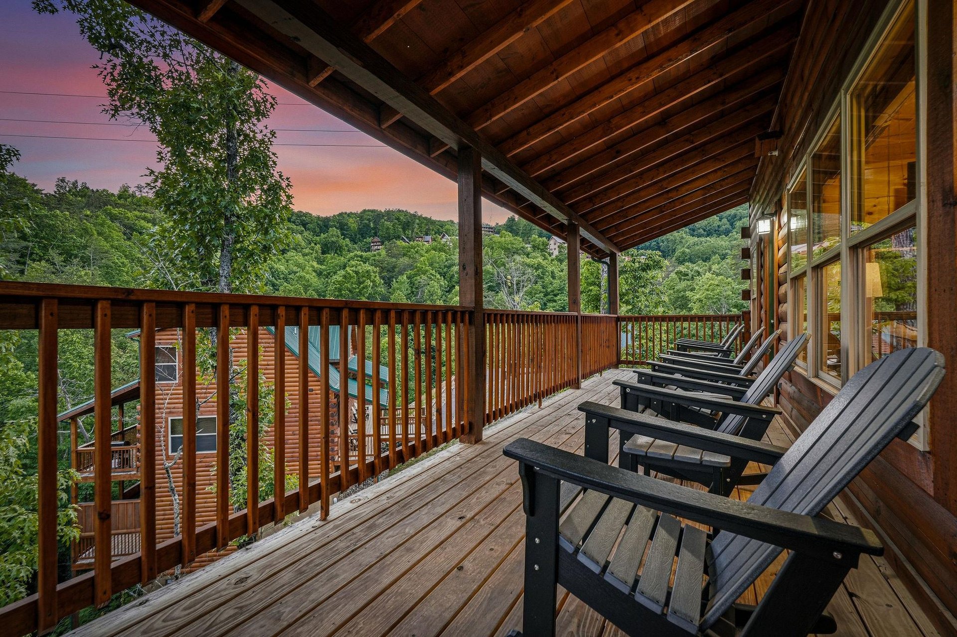 This spacious deck overlooks lush wooded hills framed by a stunning sunset sky, perfect for relaxing in comfortable Adirondack chairs and soaking in the tranquil mountain views.