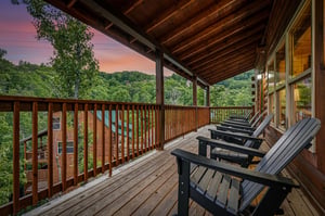 This spacious deck overlooks lush wooded hills framed by a stunning sunset sky, perfect for relaxing in comfortable Adirondack chairs and soaking in the tranquil mountain views.